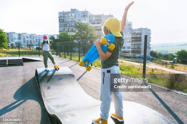 zwei kinder mit masken durch soziale trennung auf einem skateboard-park getrennt - boy skatepark stock-fotos und bilder