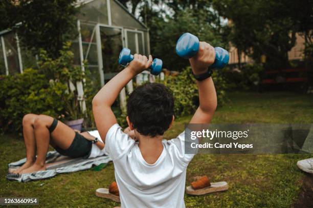 rear view boy (7) doing weights exercises in backyard with  mother - young kid and barbell stock-fotos und bilder