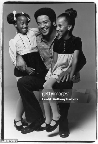 Studio portrait of American Soul and R&B musician Bill Withers as he poses with a pair of unidentified young girls, New York, New York, 1971.