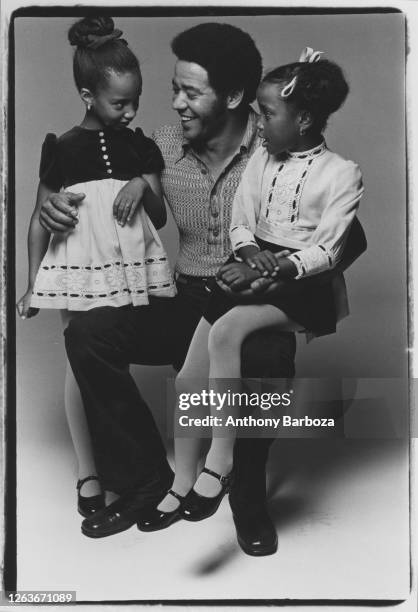 Studio portrait of American Soul and R&B musician Bill Withers as he poses with a pair of unidentified young girls, New York, New York, 1971.