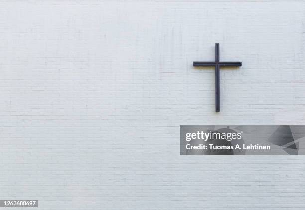 metallic cross on a white new plastered brick wall, viewed from the front. - cross christianity stock pictures, royalty-free photos & images