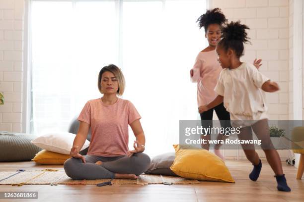 mother doing meditation yoga while daughter running around - kids meditating stock pictures, royalty-free photos & images