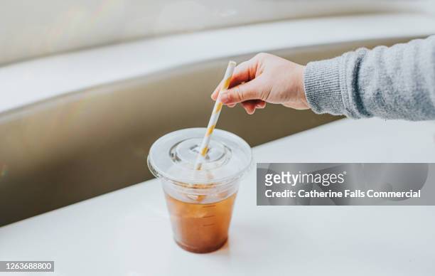 clear plastic cup half full of iced coffee, with a paper straw. hand reaches for the straw. - pressure photos et images de collection