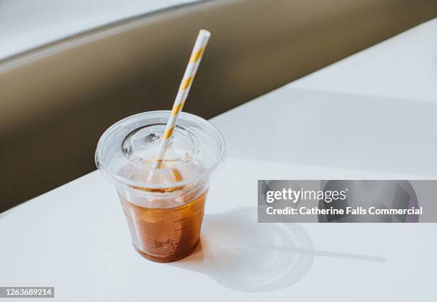 clear plastic cup half full of iced coffee, with a paper straw - deksel stockfoto's en -beelden