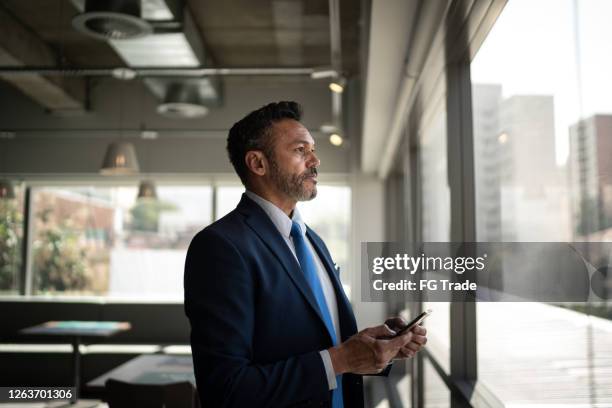 serio hombre de negocios mirando a través de la ventana - director ejecutivo de empresa fotografías e imágenes de stock