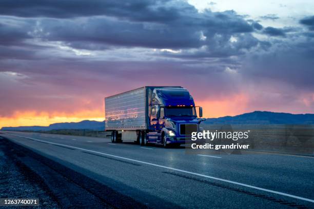 heavy hauler semi-trailer tractor truck speeding down a four-lane highway with a dramatic and colorful sunset or sunrise in the background - semi truck stock pictures, royalty-free photos & images