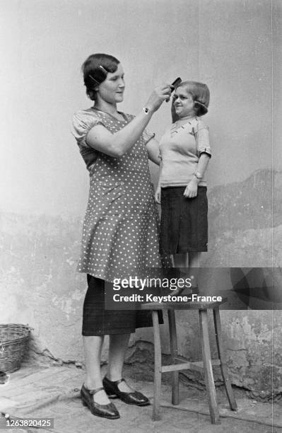 Une femme coiffant une jeune fille de petite taille en 1936 à Paris en France.