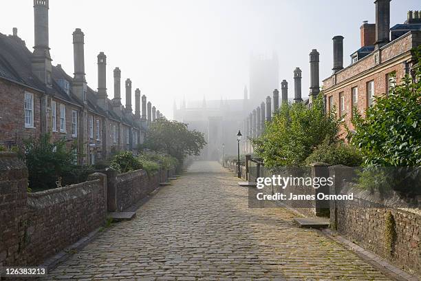 rows of terraced houses at vicars close on a misty morning with wells cathedral in the far distance in the town of wells in somerset. - adoquinado fotografías e imágenes de stock