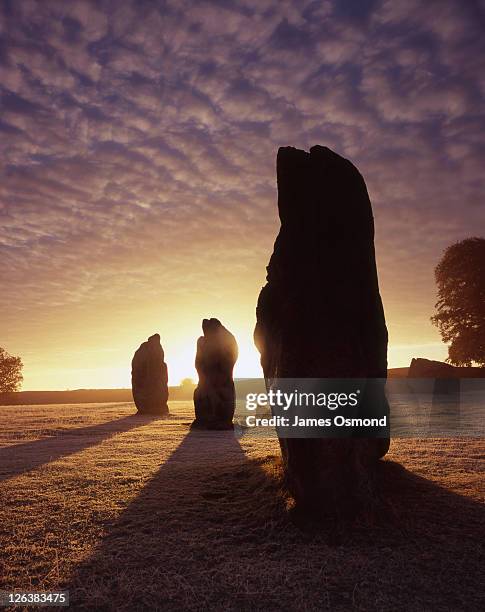 a dramatic sunrise behind the standing stones at avebury in wiltshire. - stone circle stockfoto's en -beelden