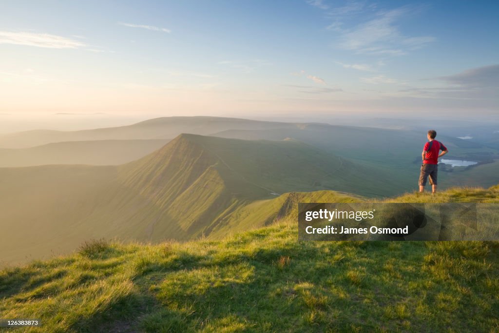 Caucasian Male Walker (30 years old) on Pen y Fan summit at sunrise looking towards Cribyn, Brecon Beacons National Park, Powys, Wales UK