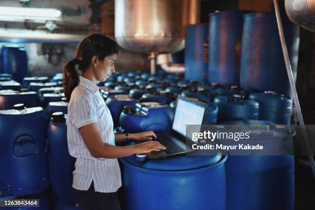 woman using laptop in the factory amongst the drum containers - india woman stock pictures, royalty-free photos & images