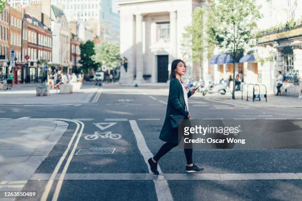 young woman with smart phone, crossing the road in the city - gehen stock-fotos und bilder