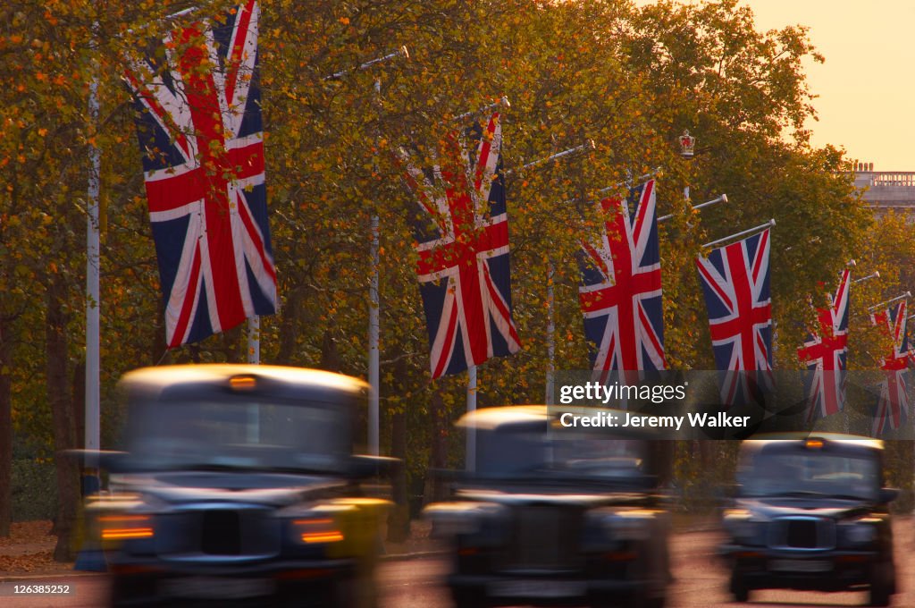 A blurred view of black London taxi cabs driving along The Mall at dusk.