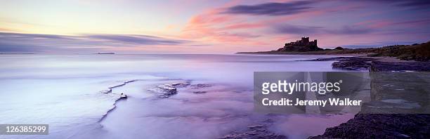 a panoramic dawn view along the coast towards bamburgh castle and the farne islands at high tide. - bamburgh castle stock pictures, royalty-free photos & images