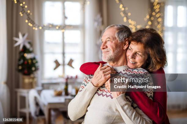 portrait of senior couple indoors at christmas time, hugging. - christmas elderly stock pictures, royalty-free photos & images