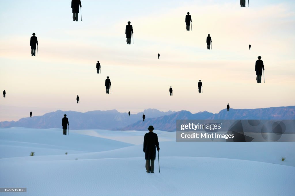 Men in bowler hats with umbrellas, outline of figures floating above ground, in a sand dune desert