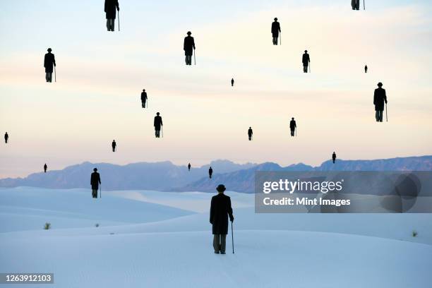men in bowler hats with umbrellas, outline of figures floating above ground, in a sand dune desert - bowler hat stock pictures, royalty-free photos & images
