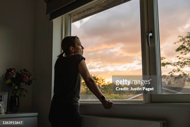 woman looking out of window at sunset - quarantäne stock-fotos und bilder