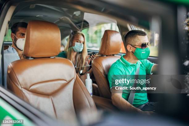 modern couple with protective face masks ridding in back seat of a taxi. - leather seats car stock pictures, royalty-free photos & images