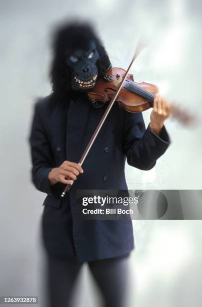 blurred image of a man in gorilla mask playing a violin outside - part of a series - masked musicians stock-fotos und bilder