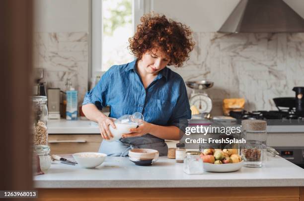 häusliches leben: frau macht haferflocken / müsli zum frühstück in der küche, natürliches licht - haferflocken stock-fotos und bilder