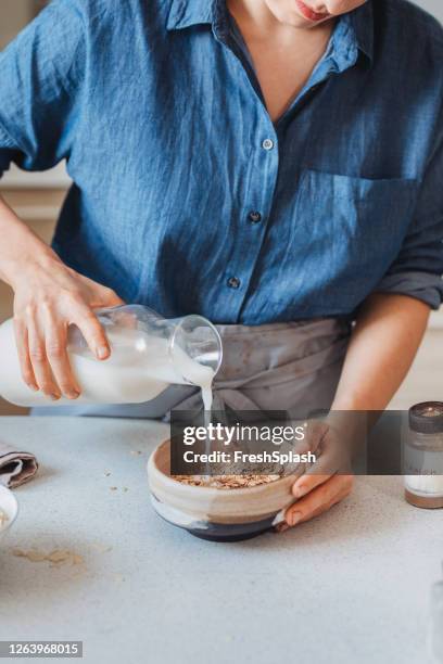 domestic life: unrecognizable woman making oatmeal/ muesli for breakfast in the kitchen, natural light - oatmeal stock pictures, royalty-free photos & images