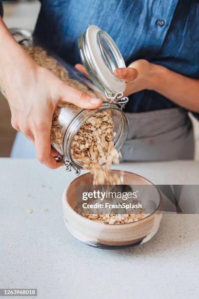 making breakfast: hände einer frau, die gerollten hafer in eine schüssel steckt - hafer stock-fotos und bilder
