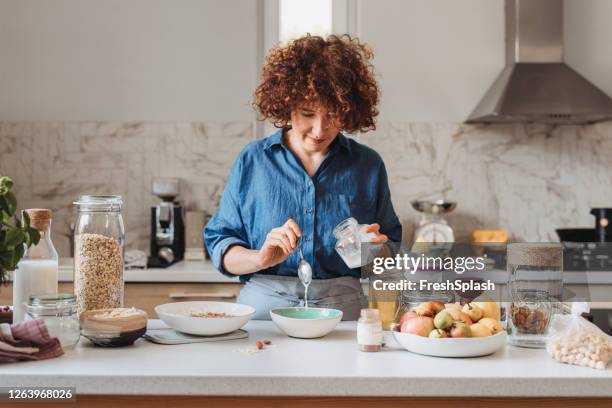 fare il muesli a casa: donna che aggiunge olio di cocco in una ciotola con avena arrotolata e spezie - fiocchi di avena foto e immagini stock