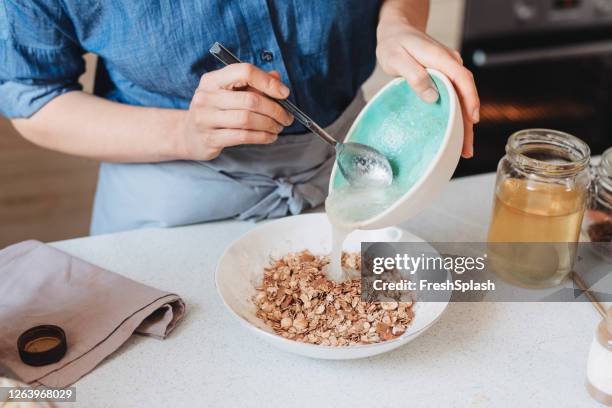 fare il muesli a casa: donna che aggiunge olio di cocco in una ciotola con avena arrotolata e spezie - coconut oil foto e immagini stock