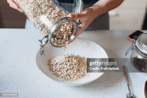 fare una colazione sana e nutriente: mani di una donna che versa avena arrotolata in una ciotola - fiocchi di avena foto e immagini stock