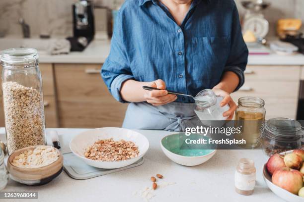 hacer granola en casa: mujer añadiendo aceite de coco en un tazón con avena y especias enrolladas - coconut oil fotografías e imágenes de stock