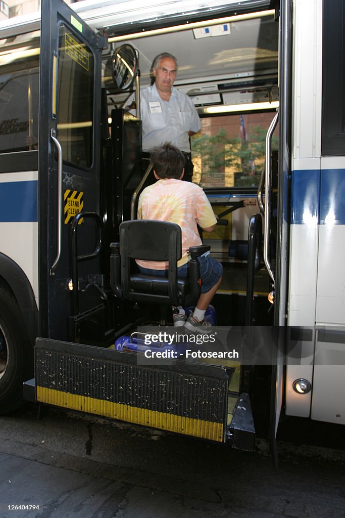 Boy with Muscular Dystrophy, utilizing a scooter/cart for mobility, getting on a city bus via a chair lift.