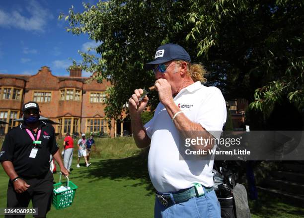 Miguel Angle Jimenez of Spain lights a cigar in front of Hanbury Manor watched by caddie Kyle Roadley ahead of the English Championship at Hanbury...