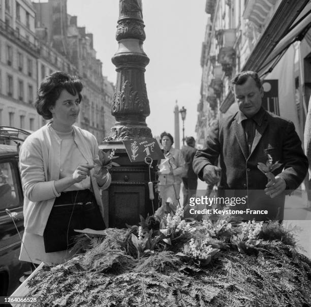 Une vendeuse prépare des petits bouquets de muguet pour le 1er mai 1966, rue de la Paix à Paris, France.