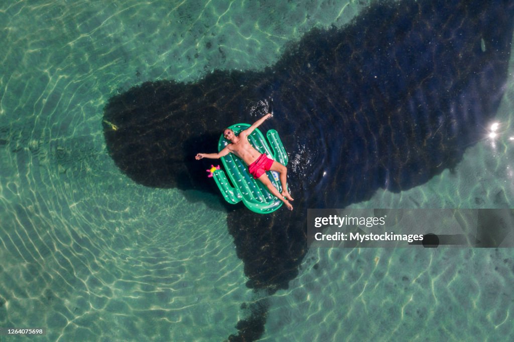 Vue aérienne de l’homme flottant sur le lac avec le bain de soleil gonflable de cactus