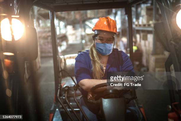 Retrato de una trabajadora que conduce carretilla elevadora en el almacén - usando máscara facial