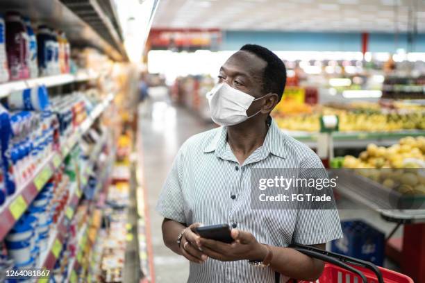 mature man using mobile and choosing products in supermarket - using face mask - black people wearing masks stock pictures, royalty-free photos & images