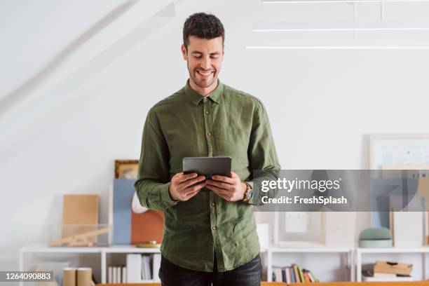 smiling man in a green shirt using a digital tablet pc in the office - green shirt stock pictures, royalty-free photos & images