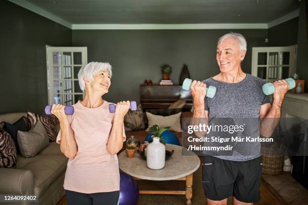 smiling senior couple lifting dumbbells together at home - hand weight stock pictures, royalty-free photos & images
