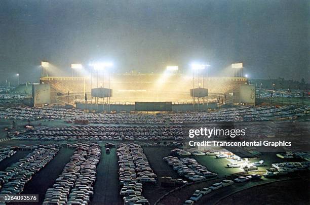 Elevated view, across the crowded parking lot, of Dodger Stadium illuminated for a night game, Los Angeles, California, circa 1970.