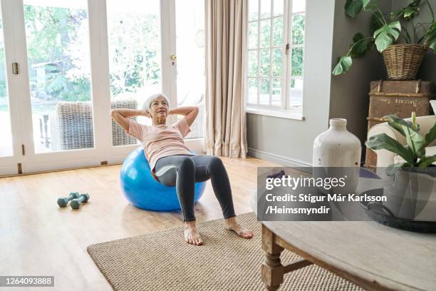 senior woman exercising on a fitness ball at home - fitness ball stock pictures, royalty-free photos & images