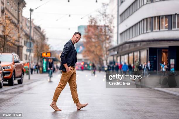 uomo scalzo che attraversa la strada della città - barefoot foto e immagini stock