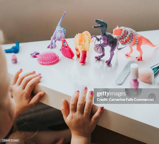child admires newly painted pink nails after beautifying toy dinosaur figurines - dinosaur toy i stock pictures, royalty-free photos & images