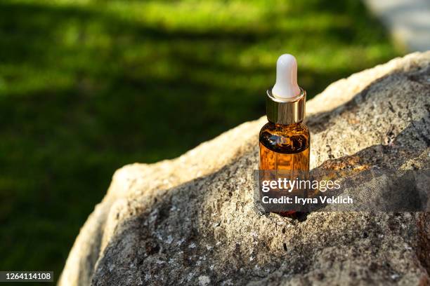 glass bottle of oil with a pipette or face serum on a stone on green grass background with sunlight. - cbd oil stock pictures, royalty-free photos & images