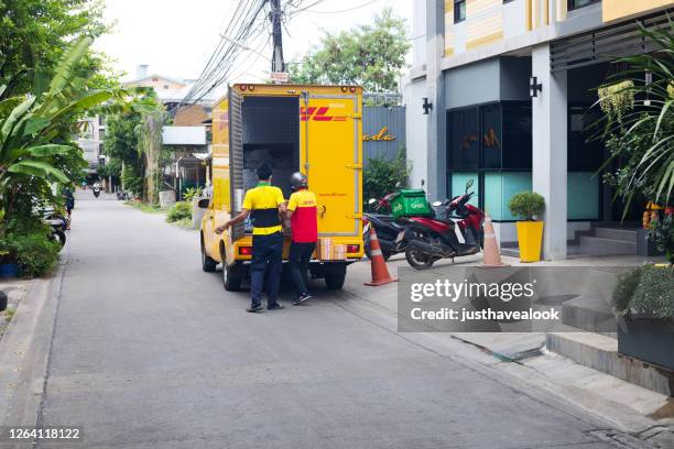 twee jonge thaise mannen en personeel zijn het laden van pakketten in dhl vrachtwagen in bangkok - auto post production filter stockfoto's en -beelden