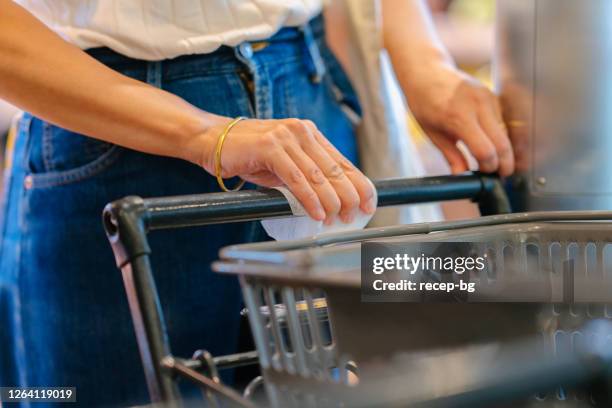 close-upfoto van de hand van de vrouw terwijl het afvegen van de oppervlakte van handvatstaaf van winkelwagentje met nat veegalcoholweefsel om te ontsmetten - bar cart stockfoto's en -beelden