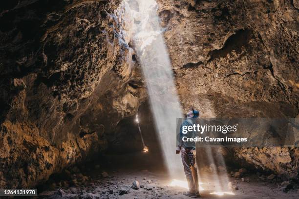 man admires a light beam that cuts through the cave - spelunking stockfoto's en -beelden