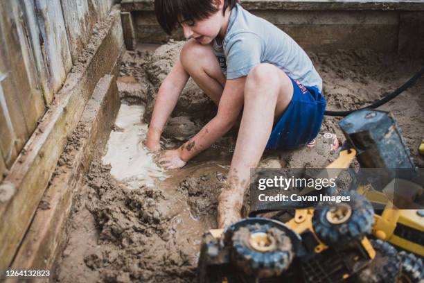 young boy playing in puddle of muddy sandbox filled with toy trucks. - 1 kid 1 sandbox stock-fotos und bilder