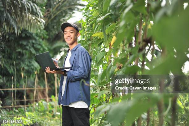 young asian farmer man holding laptop at the garden - malay archipelago stock pictures, royalty-free photos & images