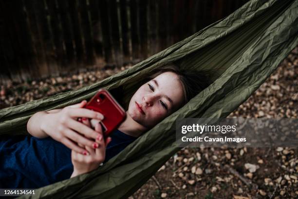 teen girl laying in hammock playing on cell phone - hammock phone stock pictures, royalty-free photos & images
